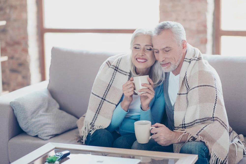 Couple plus âgé avec une couverture et une tasse de thé assis sur le canapé.