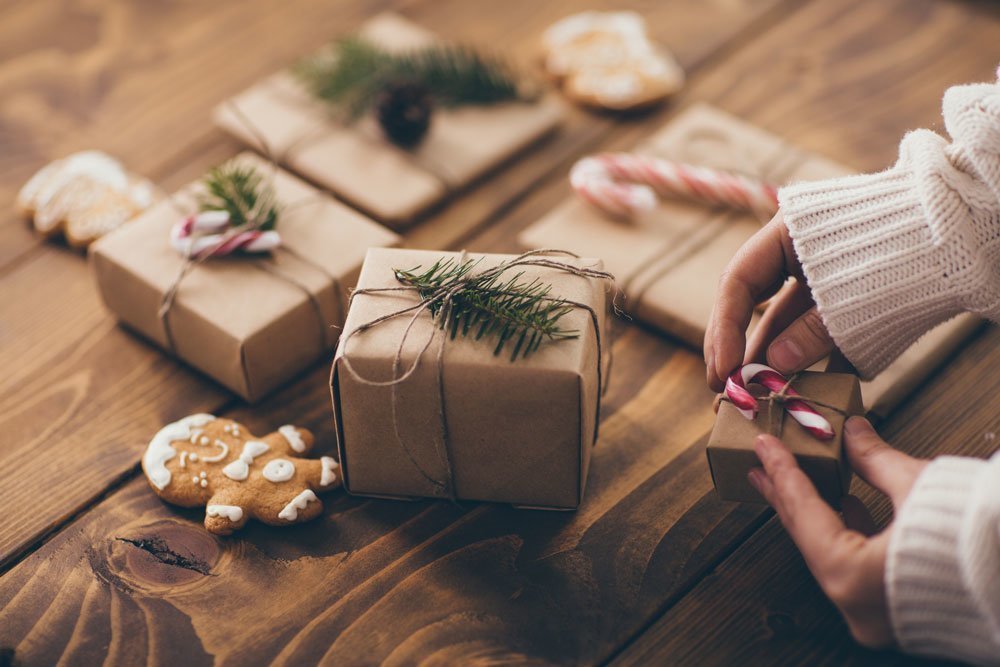 Femme qui emballe des cadeaux de Noël sur une table en bois avec des matériaux durables.